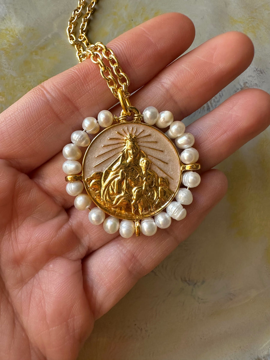Medalla de la Virgen del Carmen con perlas naturales y esmalte blanco perla en la mano